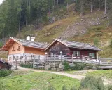 Tablander Alm a Parcines, con due baite in legno e recinzione, immerse nel verde di un pendio boscoso.