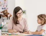 Bambina con ADHD, durante una sessione di diagnosi, disegna con una maestra sorridente.