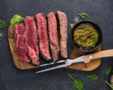 Saftiges, aufgeschnittenes Fleisch zum Grillen, serviert mit Kräutersauce und Gewürzen.