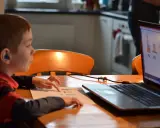 Chłopiec z niebieskim aparatem słuchowym ćwiczy wymowę sylab na lekcji logopeda online.