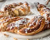 Ein goldbrauner nusskranz hefe, mit Zuckerguss und Perlen verziert, liegt auf einem Marmorsockel.