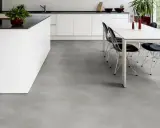 Cucina moderna con isola bianca e tavolo da pranzo. Il pavimento in LVT grigio effetto cemento completa l'ambiente minimalista.
