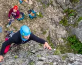 Uczestniczka kursu wspinaczkowego wspina się po skale, asekuruje ją koleżanka.