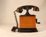 Stary telefon na korbkę z drewnianą obudową i czarną słuchawką.