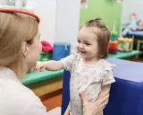 Uśmiechnięte dziecko wyciąga rączkę do terapeuty. To przykład, co to jest integracja sensoryczna – wspieranie rozwoju dziecka.
