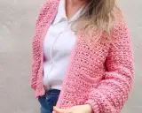 Mujer con un cardigan a crochet rosa, sobre una camisa blanca y jeans.