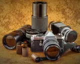 Kolekcja sprzętu fotograficznego: aparat Pentax JMC Super, obiektywy, mieszek i klisze.