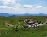 Un rifugio alpino in Lombardia, meta ideale per un trekking in giornata. Persone rilassate sui prati verdi, con montagne sullo sfondo.