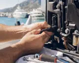 Réparation d'un panne moteur électrique sur un bateau, avec des yachts en arrière-plan.