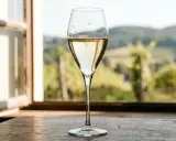 Ein Glas Champagner steht auf einem Holztisch vor einem Fenster mit Blick auf Weinberge. Der Alkoholgehalt von Champagner liegt typischerweise bei 12%.