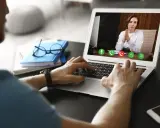 Mężczyzna prowadzi wirtualną superwizję przez laptopa. Na ekranie widać kobietę z dłońmi złożonymi w geście modlitwy.