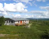Kungsleden stugor i fjällandskap med molnig himmel. Enkel träbyggnad med veranda och flaggstång.