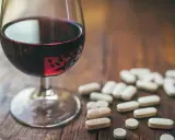 Kieliszek czerwonego wina obok garści tabletek. Leki przeciwzapalne a alkohol – potencjalne ryzyko interakcji.