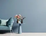 Divano blu petrolio e cuscini in tonalità pastello su sfondo azzurro polvere. Ottime idee colori pareti per un ambiente rilassante.