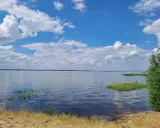 Spokojny zalew Jeziorsko w letni dzień. Błękitne niebo z białymi chmurami odbija się w tafli wody.
