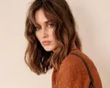 Mujer con un corte de pelo clavicut, ondas suaves y flequillo desfilado, luciendo un top marrón con lunares.