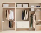 Ein aufgeräumter Kleiderschrank sortieren: Hemden, Hosen und Kleider hängen ordentlich an Kleiderbügeln. Stoffboxen und gefaltete Kleidung auf Regalen sorgen für Ordnung.