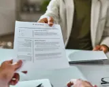 Osoba w jasnej marynarce podaje dokument CV.