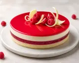 Entremet vanille et framboise, glacé rouge vif, décoré de fruits rouges et de copeaux de chocolat blanc.