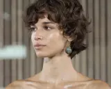 Modelo con corte media melena pelo fino, rizado y oscuro, luciendo un pendiente llamativo.