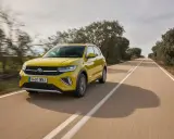 Un coche amarillo Volkswagen T-Cross circula por una carretera rural. ¿Cuánto se tarda en fabricar un coche? ¡Este parece listo para la carretera!