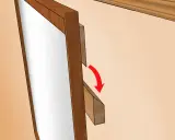 Detalle de cómo colgar un espejo. Se muestra un soporte de madera que se desliza hacia abajo para asegurar el espejo.