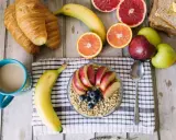 Pyszne i lekkostrawne śniadanie: owsianka z jabłkiem i jagodami, banan, croissanty, cytrusy i kawa.