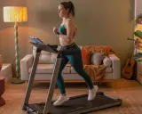 Frau trainiert auf Laufband für Gewichtsverlust. Gemütliches Wohnzimmer mit Sofa und Pflanzen.