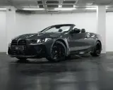 Un elegante BMW M4 negro descapotable, con sus luces LED encendidas, posa en un garaje.