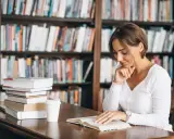 Donna legge in biblioteca, circondata da libri. La sua concentrazione è profonda, quasi come se stesse analizzando polisindeto esempi per un saggio.