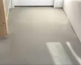 Pavimento in resina grigia, simile a un massetto, con un pilastro di legno. Potrebbe essere un'idea per pavimenti in pvc svantaggi, ma questa è una finitura grezza.