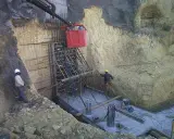 Trabajadores instalan encofrado para muro pantalla, con bataches y estructura de acero en obra.
