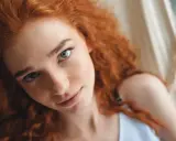 Primer plano de una joven con cabello castaño pelirrojo natural y ojos azules, recostada en una hamaca.