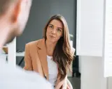 Kobieta w beżowej marynarce rozmawia z mężczyzną. Jej uśmiech sugeruje, że to miła rozmowa, być może o pracy od poniedziałku do piątku.