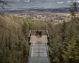 Dwie osoby stoją na szklanym tarasie widokowym, podziwiając panoramę Starego Sącza i okolic.