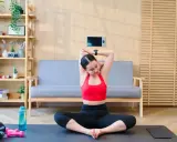 Frau dehnt sich im Schneidersitz, ein wichtiger Teil ihres Mobility Trainings. Trainingsmatte, Wasserflasche und Hanteln liegen bereit.