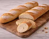 Deux baguettes dorées, l'une coupée en tranches, sur une planche en bois. Parfait pour une recette baguette croustillante et aérée.