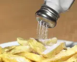 Salzstreuer rieselt Salz auf Pommes. Zu viel Salz essen kann zu Problemen führen.