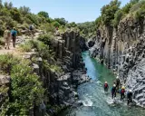 Escursionisti ammirano le spettacolari **cascate gole dell'Alcantara**, mentre un gruppo fa canyoning nel fiume.