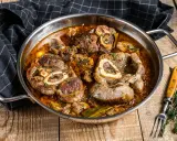 Ossobuco que es: jugosas rodajas de ternera cocinadas a fuego lento en una rica salsa con hierbas y especias, servidas en una sartén metálica.