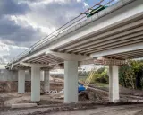 Construcción de un puente de viga con pilares de hormigón y grúa amarilla en el sitio.