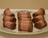 En tallrik med rosa marsipanbakelser doppade i choklad. Dessa små godsaker, som ser ut som en dammsugare i långpanna, är redo att avnjutas.