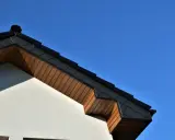 Elegancka podbitka z płyty OSB pod ciemnym dachem, kontrastująca z jasną elewacją i błękitem nieba.