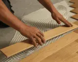 Man's hands carefully placing a wooden plank during the installation of floating flooring.