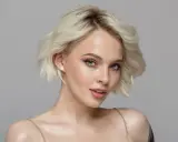 Mujer joven con cabello rubio platino y piel clara, con pecas sutiles y ojos azules penetrantes.