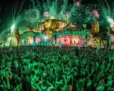 Folla immensa sotto un palco spettacolare con fuochi d'artificio verdi, uno dei rave party più famosi al mondo.