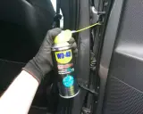 Ręka w rękawiczce aplikuje smar do zawiasów drzwi samochodowych WD-40 Specialist.