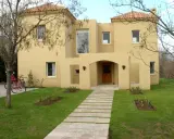 Una encantadora casa color arena con techo de tejas rojas, un camino de losas y dos bicicletas aparcadas en el jardín.