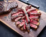 Una succulenta fiorentina alla griglia, affettata e servita su un tagliere di legno, con sale grosso sparso.