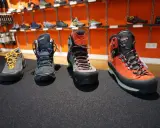 Vier Paar Wanderschuhe in verschiedenen Kategorien, von leichten Zustiegsschuhen bis zu robusten Bergstiefeln, stehen auf einem dunklen Teppich.